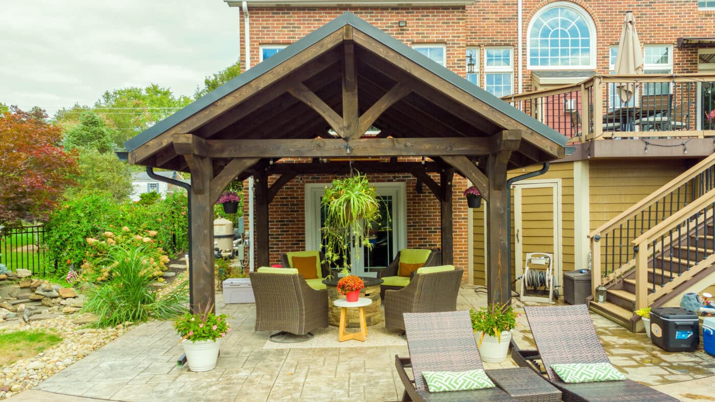 The Vista A-Frame Pavilion in a backyard with seats and plants hanging underneath